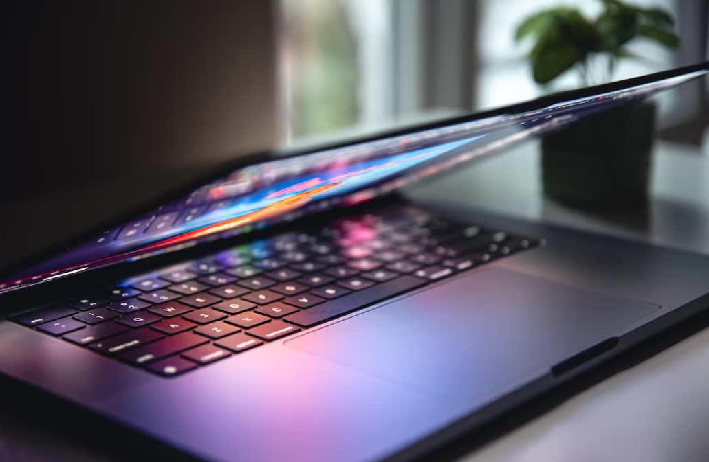 semi-closed laptop on the table, small vase with flower on it